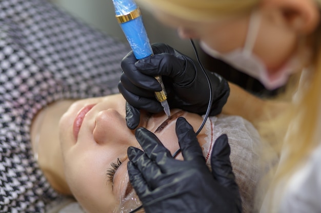 El flujo de trabajo de las cejas microblading en un salón de belleza. Mujer que tiene sus cejas teñidas. Maquillaje semipermanente para cejas. Centrarse en la cara y la ceja de la modelo