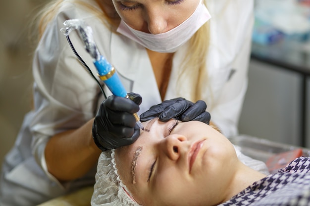 El flujo de trabajo de las cejas microblading en un salón de belleza. Mujer que tiene sus cejas teñidas. Maquillaje semipermanente para cejas. Centrarse en la cara y la ceja de la modelo