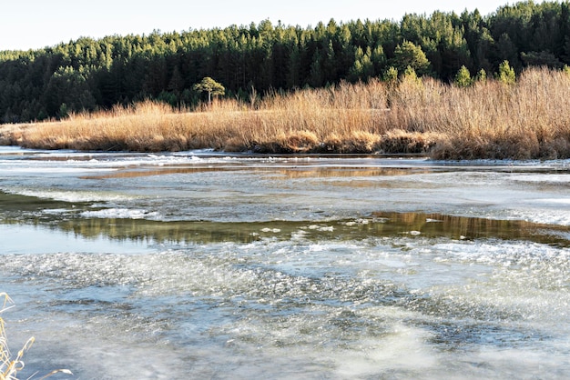 Fluss bedeckt mit dem ersten Eis und Schnee im Spätherbst oder frühen Winter gegen Waldlandschaft