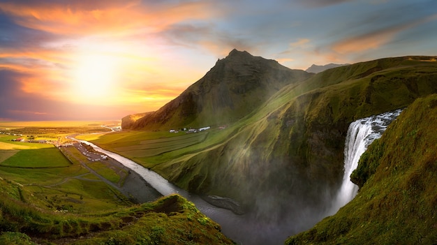 Fluss, der von einem Wasserfall in Island abfließt, umgeben von Bergen bei Sonnenuntergang