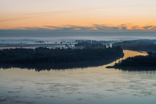 Flussufer mit Wald unter Himmel vor dem Morgengrauen