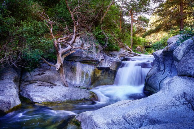 Flusswasserfall zwischen Felsen bei Sonnenaufgang und Holzbrücke im Hintergrund. Navacerrada.