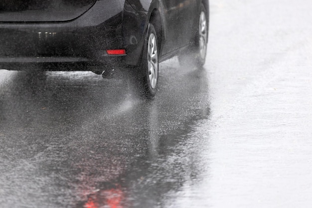 Fluxo de respingos de água da chuva das rodas do carro preto movendo-se rapidamente na cidade à luz do dia com foco seletivo