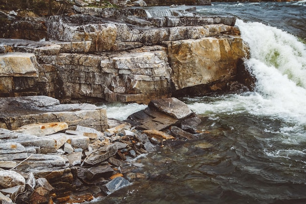 Fluxo no rio de montanha rápido de leito de pedra entre rochas água ferve em redemoinhos de corrente