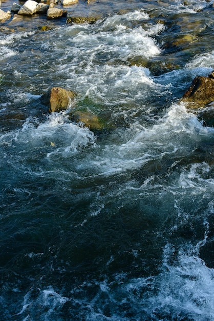 Fluye por un río tormentoso entre las rocas en el parque de otoño en un día cálido