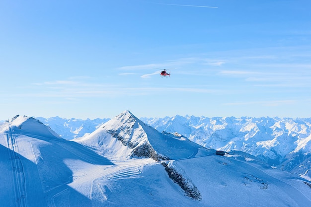 Flying Red Helicopter sobre la estación de esquí Hintertux Glacier en Zillertal en Tirol en Austria en invierno en los Alpes. Chopper y montañas alpinas con nieve. Aviones y cielo azul y laderas blancas.