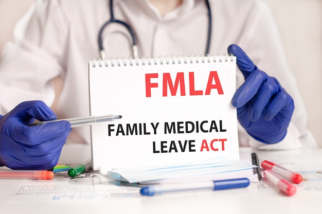 FMLA-Karte in Händen des Arztes. Arzthände in blauen Handschuhen halten ein Blatt Papier mit Text FMLA - Abkürzung für Family Medical Leave Act, medizinisches Konzept.