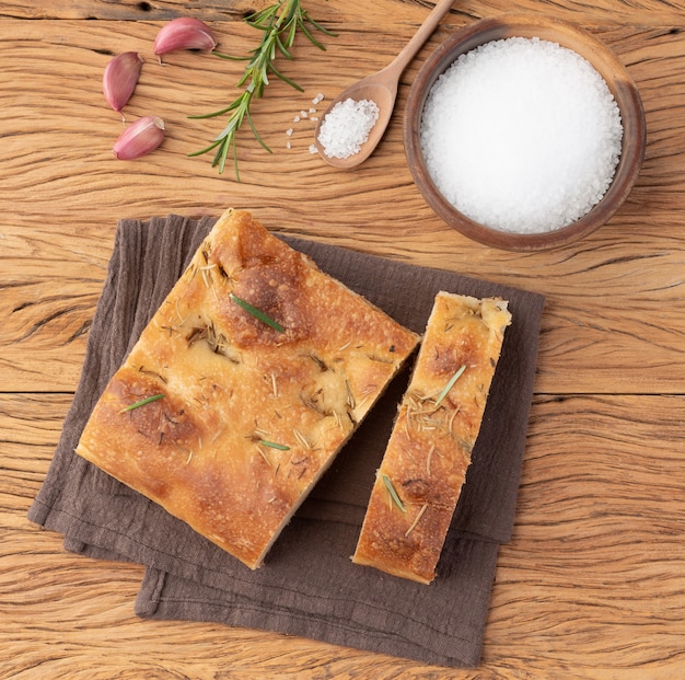 Focaccia caseira com sal, alho e alecrim sobre mesa de madeira.