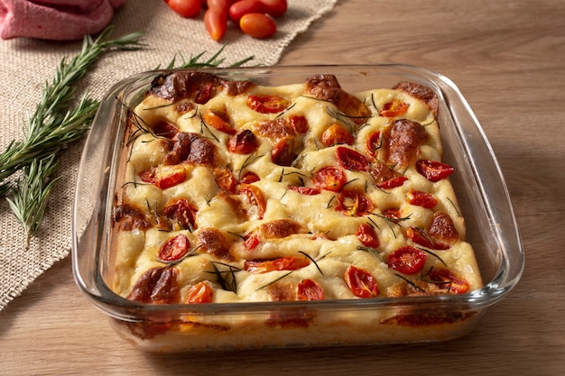 Focaccia com alecrim, azeite e tomate na mesa de madeira.