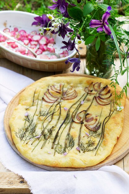 Focaccia com cebola, rabanete assado e um buquê de flores em uma mesa de madeira