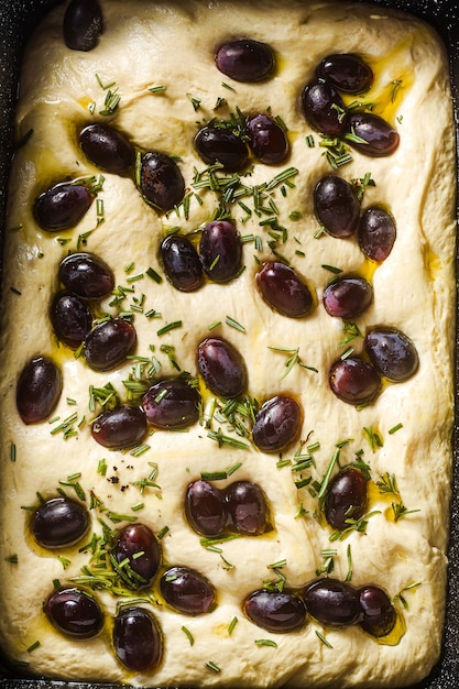 Focaccia cruda con uvas rojas sobre una mesa azul en una bandeja para hornear.