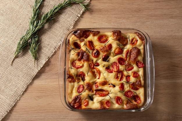 Focaccia de Pugliese italiana caseira com alecrim, azeite e tomate na mesa de madeira.