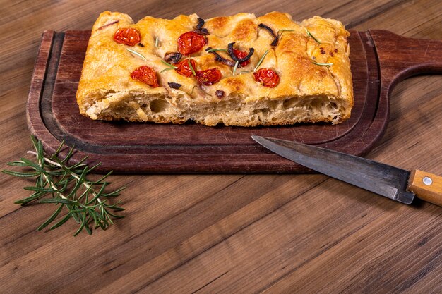 Foto focaccia italiana tradicional com tomate cereja, azeitonas pretas e alecrim.