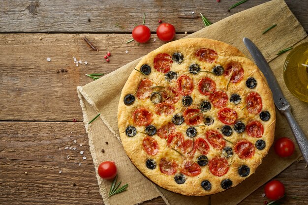 Focaccia, Pizza, italienisches flaches Brot mit Tomaten, Oliven und Rosmarin auf hölzerner rustikaler Tabelle