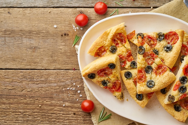 Focaccia, Pizza, Scheiben des italienischen Fladenbrotes mit Tomaten, Oliven und Rosmarin auf hölzernem