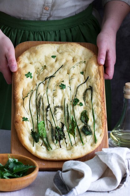 Focaccia vegana feita de massa de levedura com várias ervas mantidas por uma mulher. Estilo rústico.