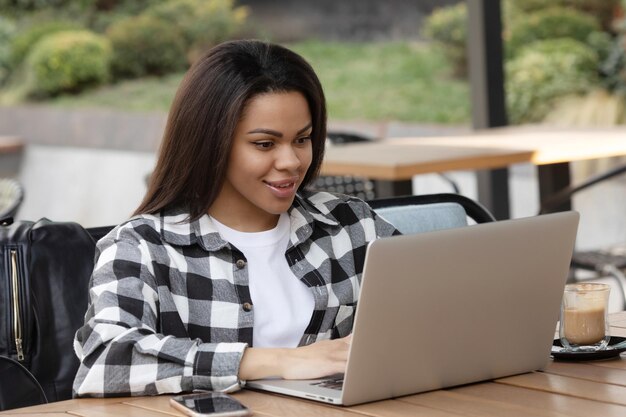 Focada jovem africana sentada sozinha em um balcão em um café trabalhando em um laptop