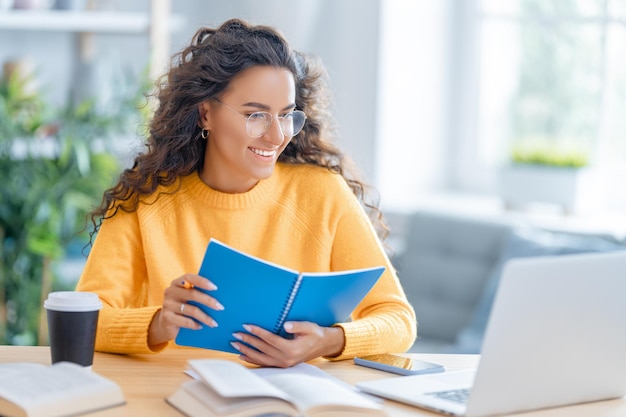 Focada jovem empresária estudando online, assistindo webinar, podcast no laptop, fazendo anotações, sentado na mesa de trabalho. Conceito de e-learning.