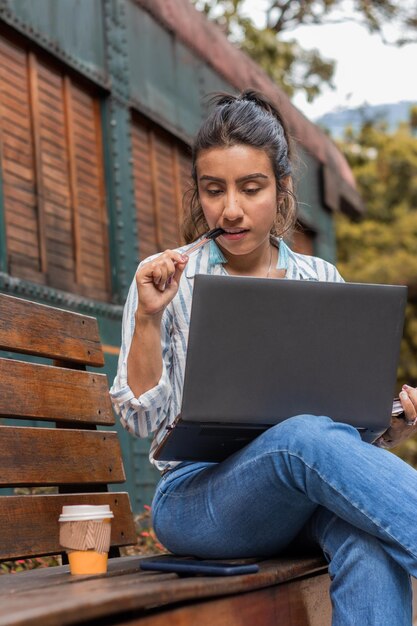 Focada jovem morena pensando usando o laptop estudando no parque