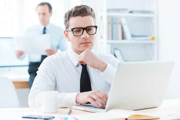 Focado em seu trabalho. empresário atencioso em trajes formais, trabalhando em um laptop e segurando a mão no queixo