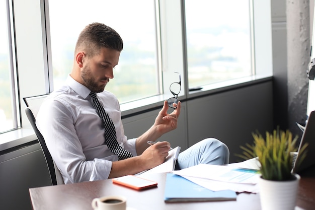 Focado empresário moderno trabalhando e tomando notas em seu escritório moderno.