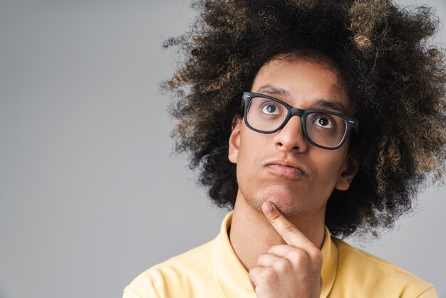 Foto focado homem caucasiano com penteado afro usando óculos pensando e olhando para cima, para copyspace isolado sobre a parede cinza