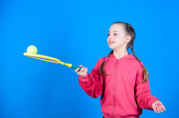 Focado na bola Lazer ativo e hobby Tênis esporte e entretenimento Menina adorável criança brincar de tênis Praticar habilidades de tênis e se divertir Raquete de tênis de criança atleta em fundo azul