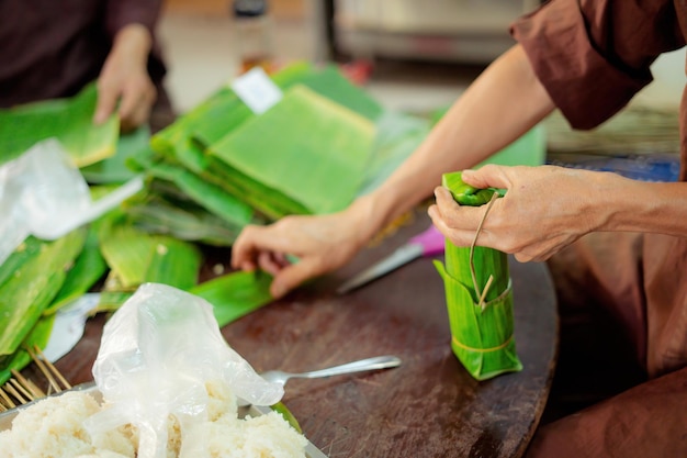 Foco anciana con vestido tradicional vietnamita ao ba ba Hacer envoltura Tet Cake el año nuevo lunar vietnamita Tet comida al aire libre con las manos