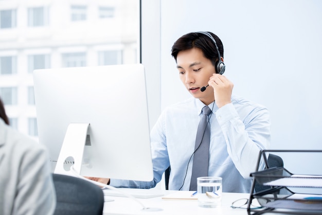 Foco asiático bonito homem trabalhando no escritório de call center como um operador de telemarketing