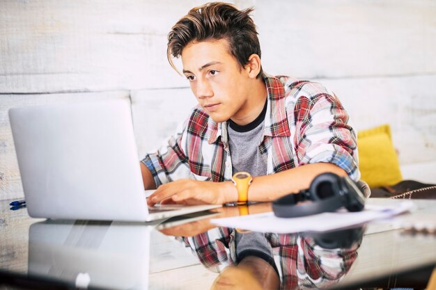 Foto foco de adolescente bonito para seus estudos fazendo lição de casa em casa na mesa com o laptop ou computador - fones de ouvido na mesa - conceito de estilo de vida indor - cara escrevendo e lendo