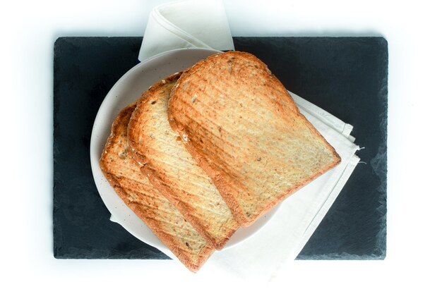 Foto foco de vista superior da pilha de fatias de pão torrado em uma única placa preta sobre fundo branco puro