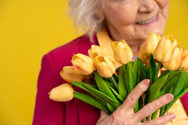 Foco do buquê de tulipas amarelas nas mãos de uma mulher idosa sorridente e turva