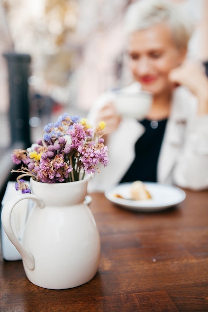 En el foco de un jarrón de flores detrás de una mujer tomando café en el fondo