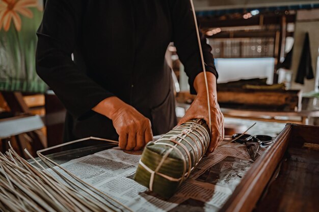 Foco mulher velha com vestido tradicional vietnamita ao ba ba Fazendo embrulho Tet Cake o ano novo lunar vietnamita Tet food ao ar livre pelas mãos