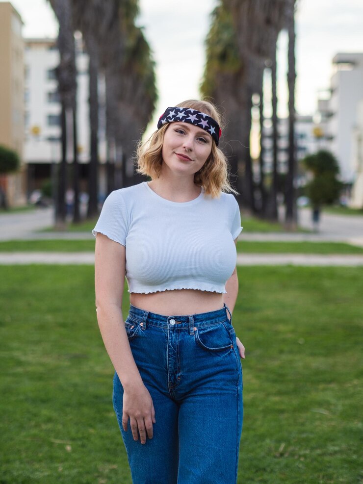 Foto foco raso de uma linda mulher caucasiana em uma bandana da moda e top de colheita posando em um parque