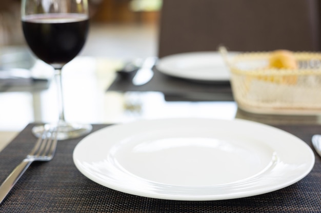 Foto foco selectivo de la vajilla limpio conjunto plato blanco tenedor y cuchara con un vaso de vino tinto