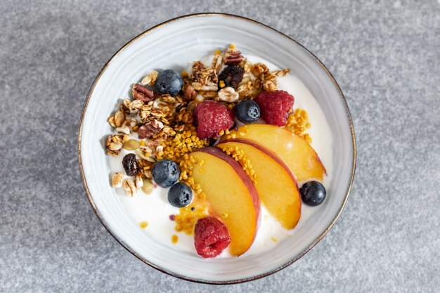 Foco selectivo de la vista superior del granola con el melocotón fresco del yogur griego, arándano, frambuesa