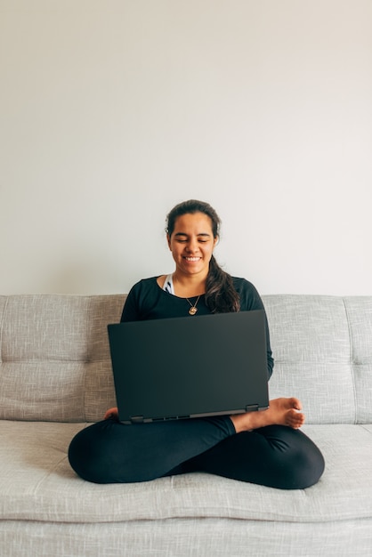 Foco seletivo a imagem vertical de uma mulher latina sentada de pernas cruzadas na mobília de sua casa, bebendo e assistindo a uma aula de ioga online. conceito de estar em casa