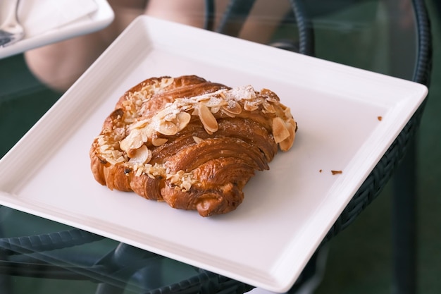 Foto foco seletivo croissant fresco com fatia de amêndoa por cima na placa branca no café da manhã do hotel, padaria e bar de pastelaria, torrada francesa tradicional, pastelaria, torrada de amêndoa com fundo de café