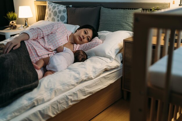 foco seletivo cuidando da mãe asiática acordada na cama de pijama está amamentando seu bebê recém-nascido com leite materno na hora de dormir no quarto em casa.
