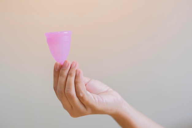 Foco seletivo da mão da mulher segurando o copo menstrual sobre um fundo bege claro