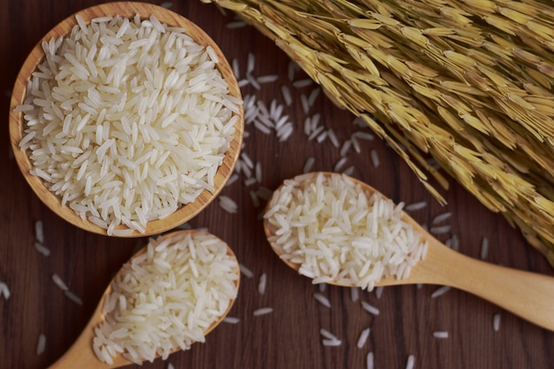 Foto foco seletivo de arroz de jasmim tailandês em uma tigela de madeira clara e colheres com orelha de arroz