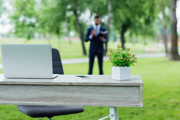 Foco seletivo de mesa com vaso de flores e laptop no parque