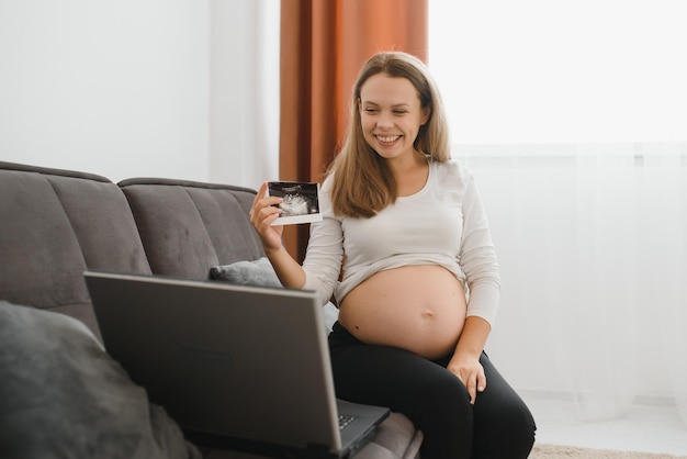 Foco seletivo de mulher grávida alegre mostrando fotos de ultrassom durante uma videochamada