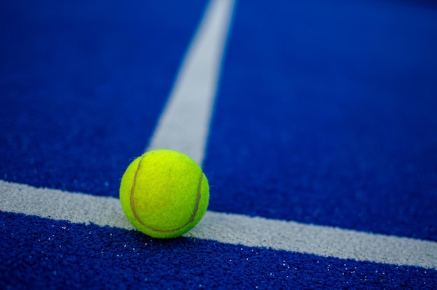 foco seletivo de uma bola na linha branca de uma quadra de paddle azul. conceito de esportes