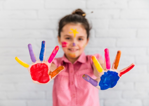 Foto foco seletivo de uma garota mostrando as mãos pintadas coloridas