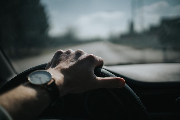 Foco seletivo de uma mão masculina com um relógio de pulso segurando o volante de um carro