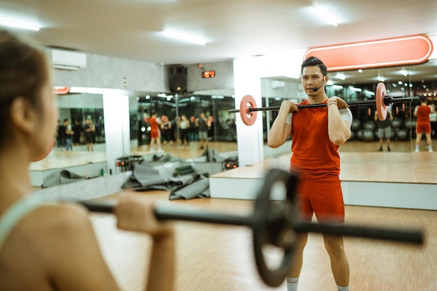 Foto foco seletivo do instrutor masculino levantando barra durante o exercício em grupo na sala de fitness