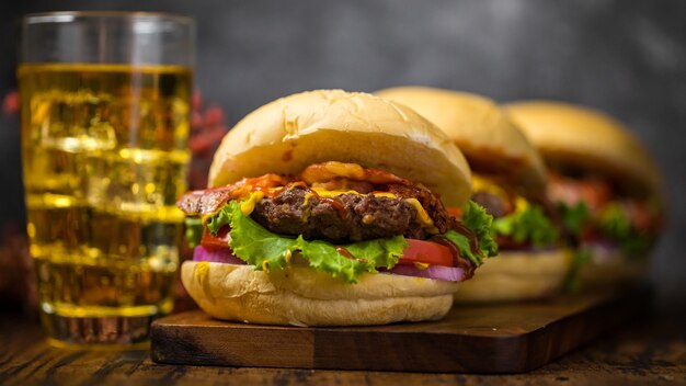 Foco seletivo em hambúrgueres com carne bovina, cebola frita, espinafre, ketchup e queijo. servido com cerveja no fundo do loft da placa de madeira.