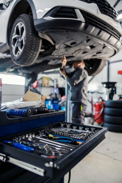 Foto foco seletivo em uma gaveta com ferramentas de automecânica com trabalhador consertando carro